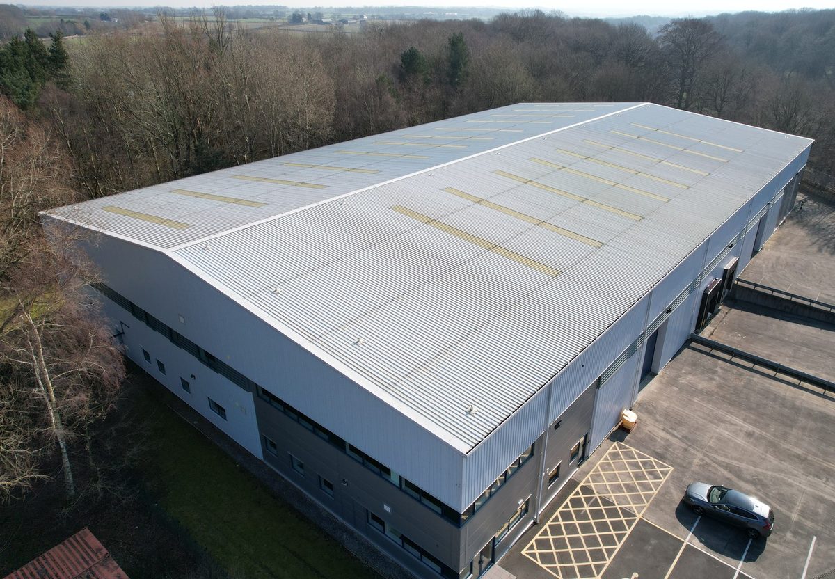 An industrial unit's profiled metal roof from above, lines of patch repairs visible